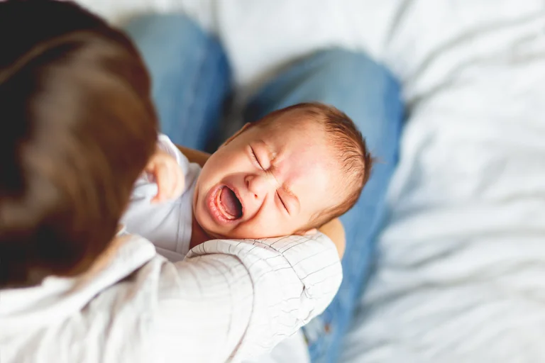 Weinendes Baby auf dem Arm eines Elternteils.