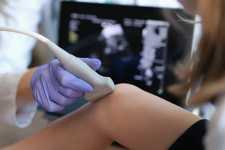 Arzt führt eine Ultraschalluntersuchung am Knie eines Kindes durch, während das Bild auf dem Bildschirm angezeigt wird.