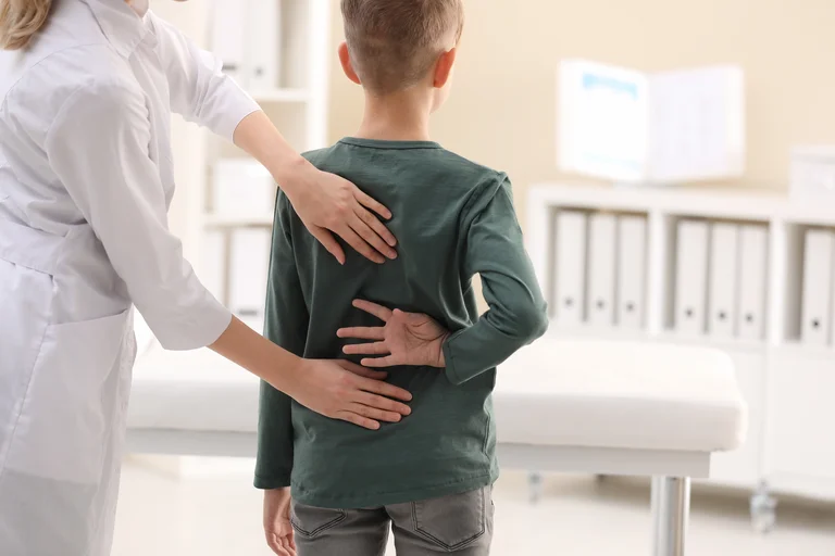 Ärztin tastet den Rücken eines Jungen ab.
