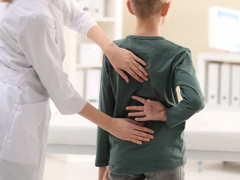 Ärztin tastet den Rücken eines Jungen ab.