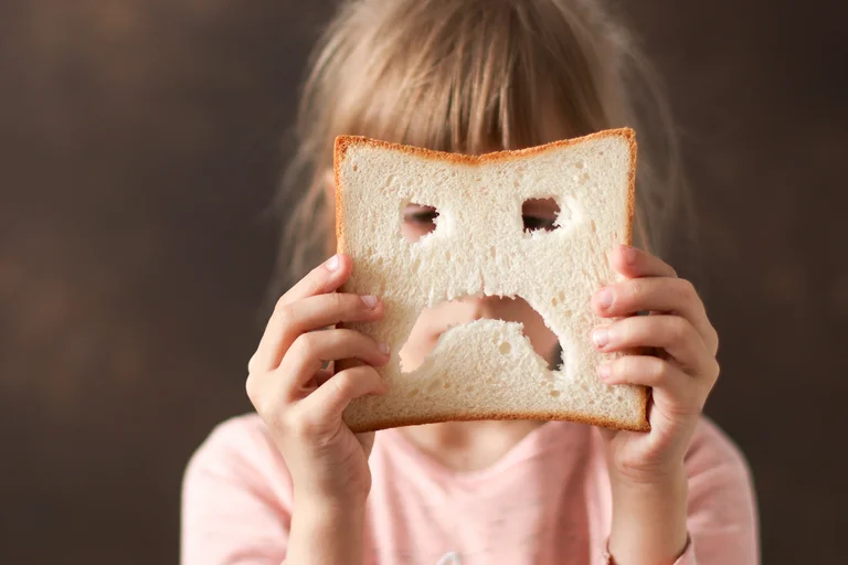 Mädchen hält ein Stück ausgehöhltes Brot, das wie ein trauriges Gesicht aussieht.
