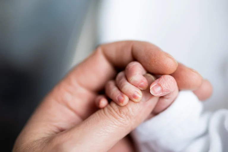 Neugeborenes Baby hält die Hand eines Erwachsenen.