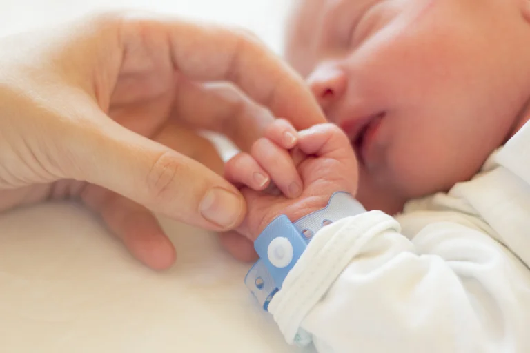 Neugeborenes Baby hält die Hand einer Person, während es ein blaues Identifikationsarmband trägt.