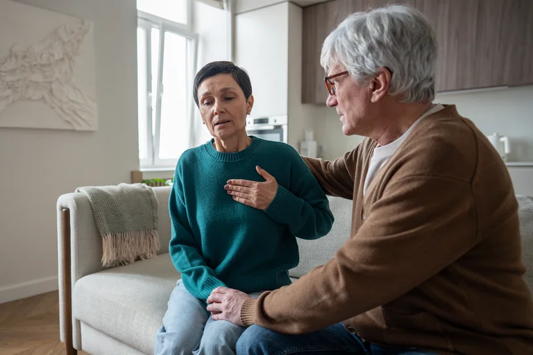 Eine Frau mit besorgtem Gesichtsausdruck hält sich die Brust, während ein Mann sie beruhigend berührt. Das Bild symbolisiert die Risiken von Carotisstenose und Schlaganfall durch Faktoren wie Bluthochdruck und Diabetes.