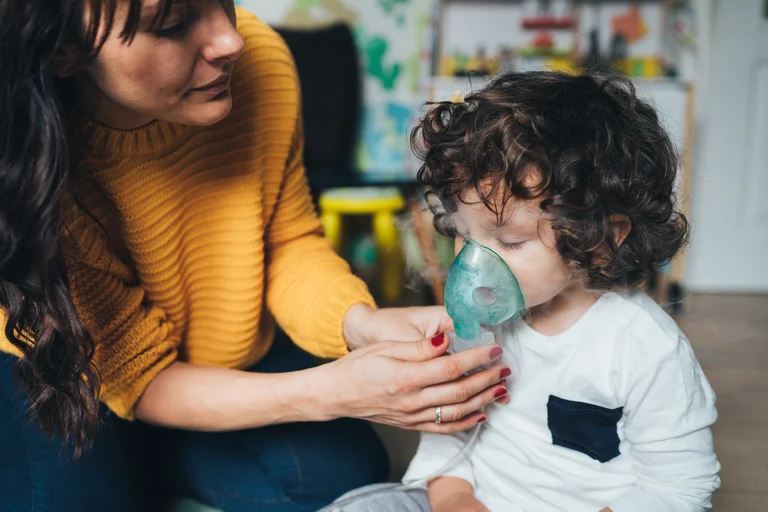 Kind erhält eine Inhalationstherapie mit einem Inhalator, während eine Person ihm hilft.