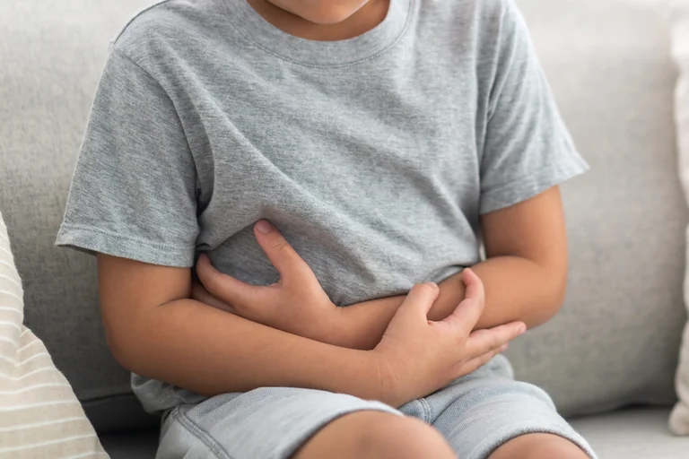 Kind mit Bauchschmerzen, das sich den Bauch hält und auf der Couch sitzt.