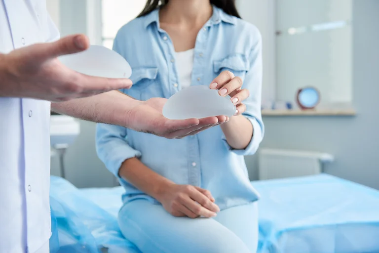 Arzt zeigt einer Patientin verschiedene Implantate, die für eine Brustvergrößerung infrage kommen