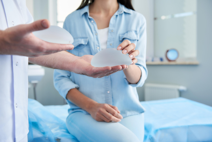 Arzt zeigt einer Patientin verschiedene Implantate, die für eine Brustvergrößerung infrage kommen